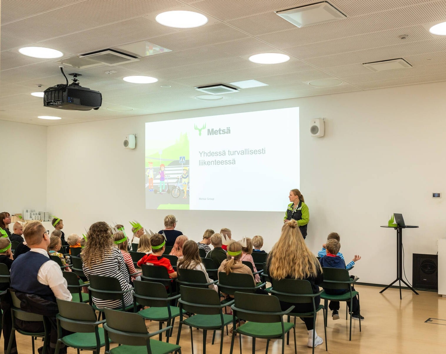 Children take part in a traffic safety presentation at Metsä Fibre’s Äänekoski bioproduct mill. The session focuses on safe behaviour in traffic, and participants follow a presentation displayed on a projection screen.