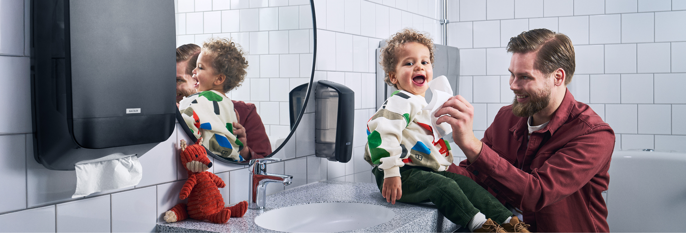 Vuxen som torkar ett barns ansikte inne på en offentlig toalett.