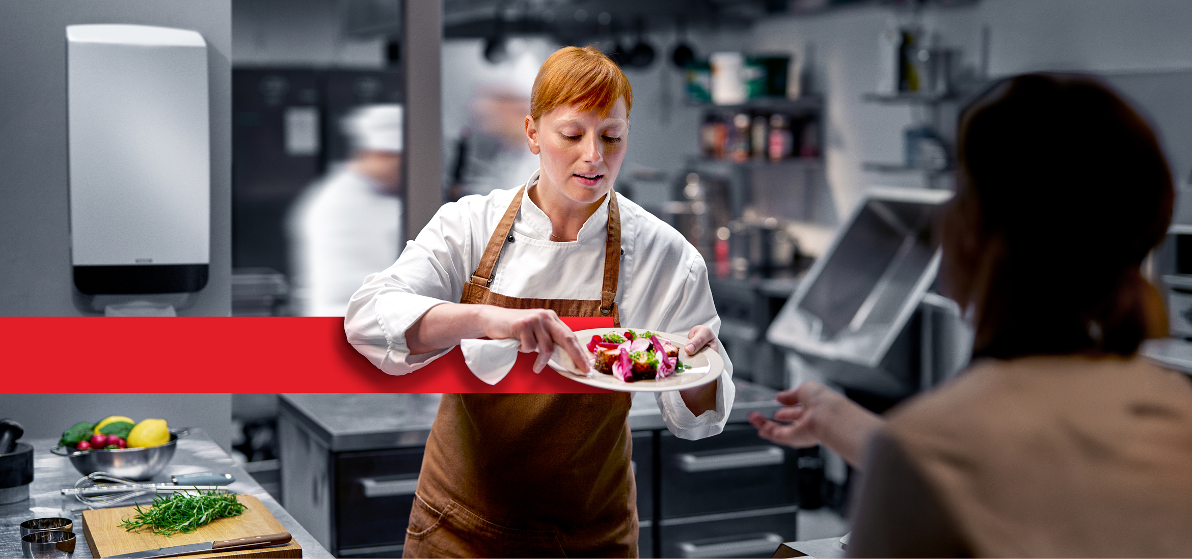 Person i arbetskläder som torkar en tallrik med mat i ett restaurangkök.