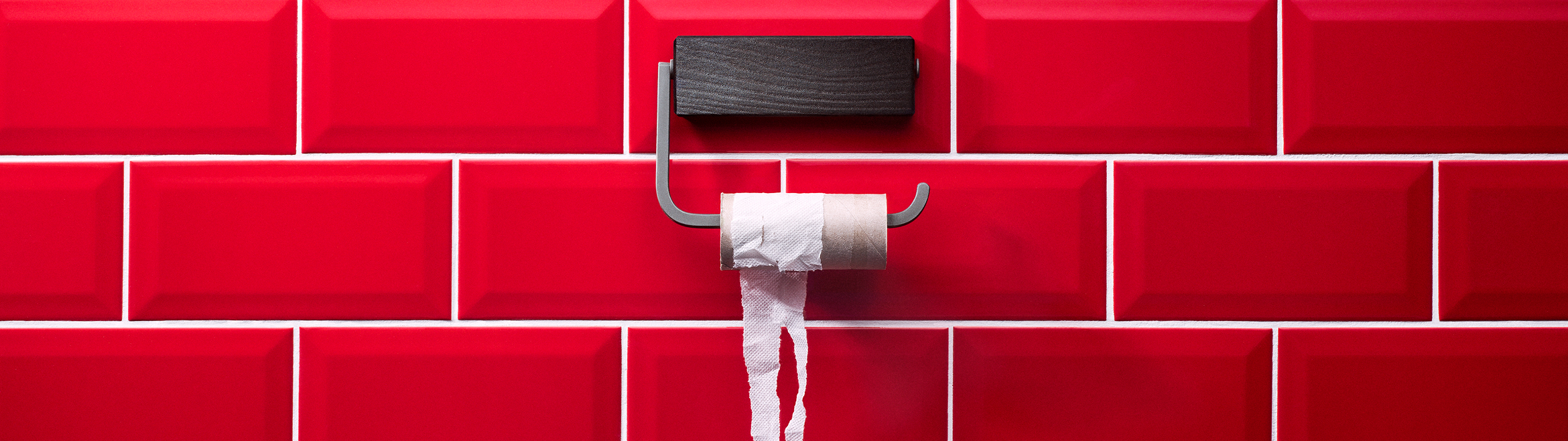 Tom toalettrulle på hållare framför röda kakelplattor i ett hygienutrymme.