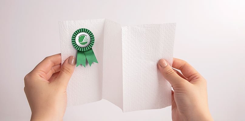 Två händer håller upp ett mjukpapper med Svanenmärket, symbol för miljökrav och kvalitet.