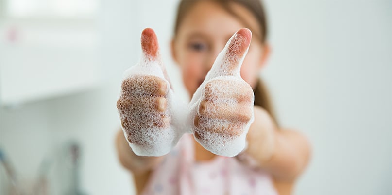 Barn visar upp löddriga händer och ger tummen upp – symbol för god handhygien och miljömärkt tvål.
