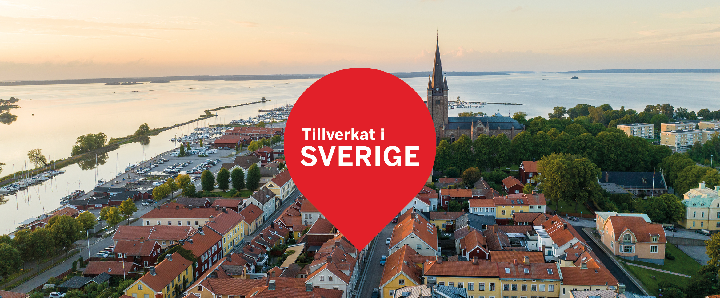 Flygfoto &ouml;ver Mariestad med en r&ouml;d platsmark&ouml;r som s&auml;ger "Tillverkat i Sverige", vilket signalerar lokal produktion.