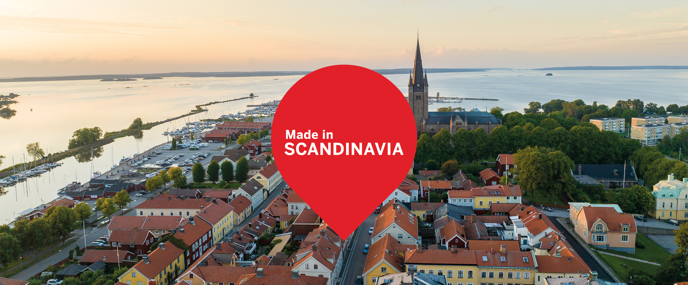 Luftfoto av en skandinavisk småby ved vannet, med en rød markør og teksten "Made in SCANDINAVIA" midt i bildet.