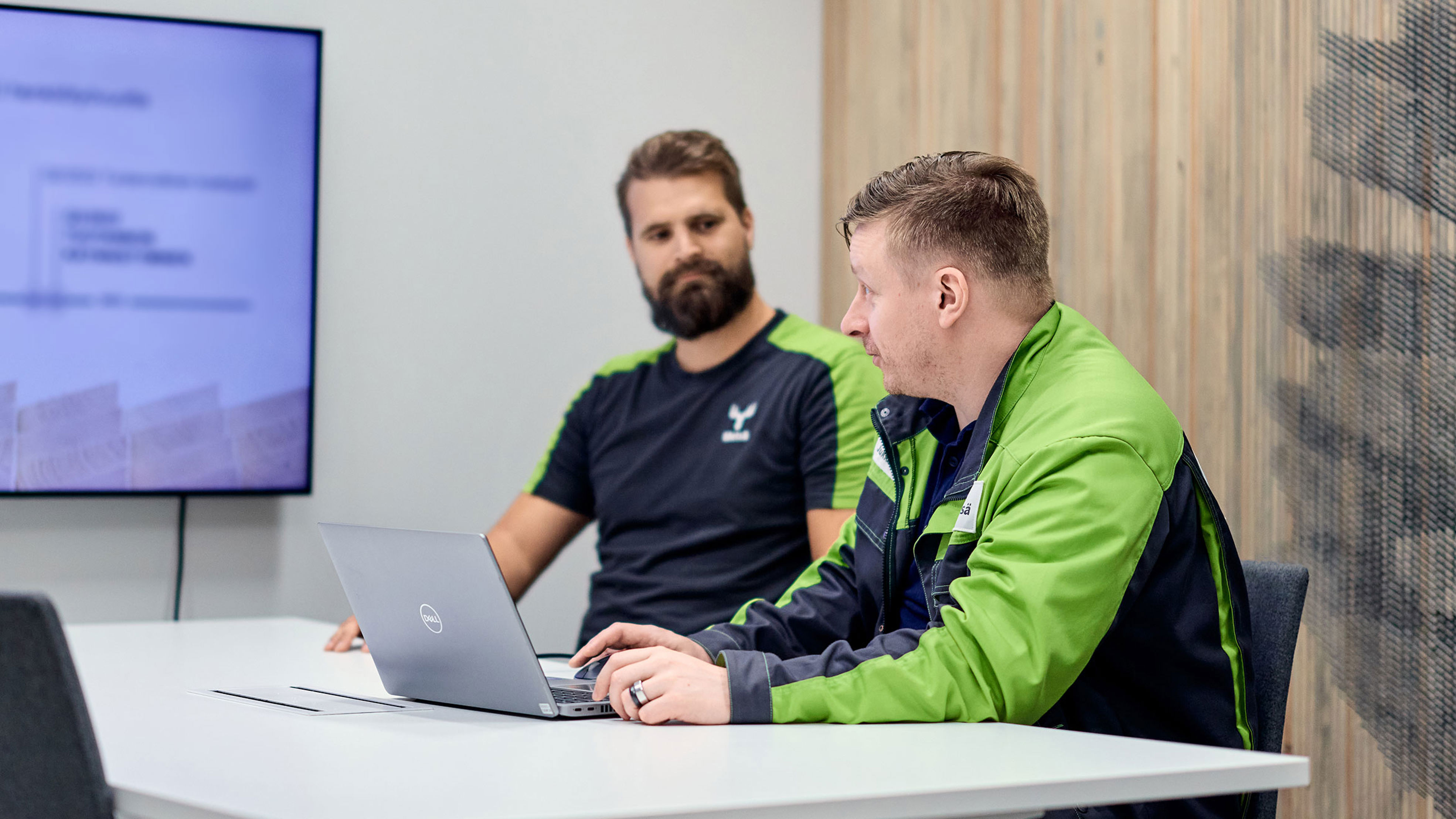 Two men in a meeting room with a laptop and a presentation on screen