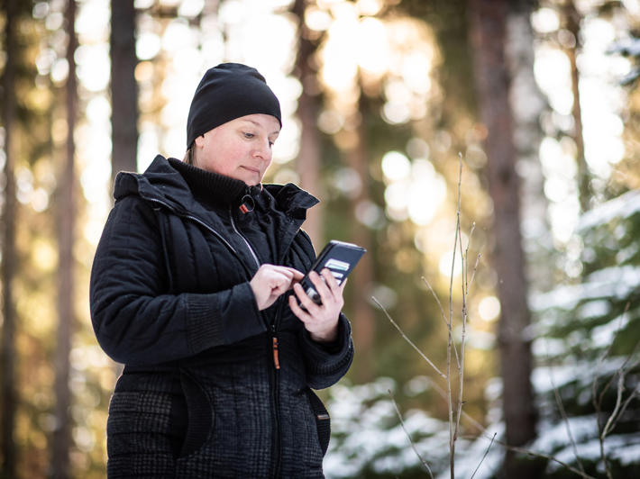 Nainen seisoo metsässä puhelin kädessä