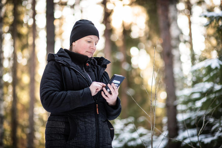 Nainen seisoo metsässä puhelin kädessä