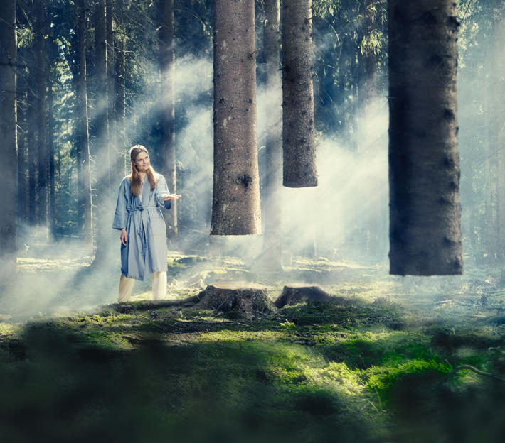 Kvinna står i disig skog, träden svävar i luften.
