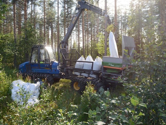 Skogstraktor tömmer gödselsäck i spridare.