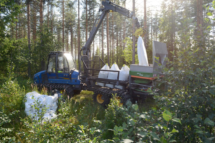 Skogstraktor tömmer gödselsäck i spridare.