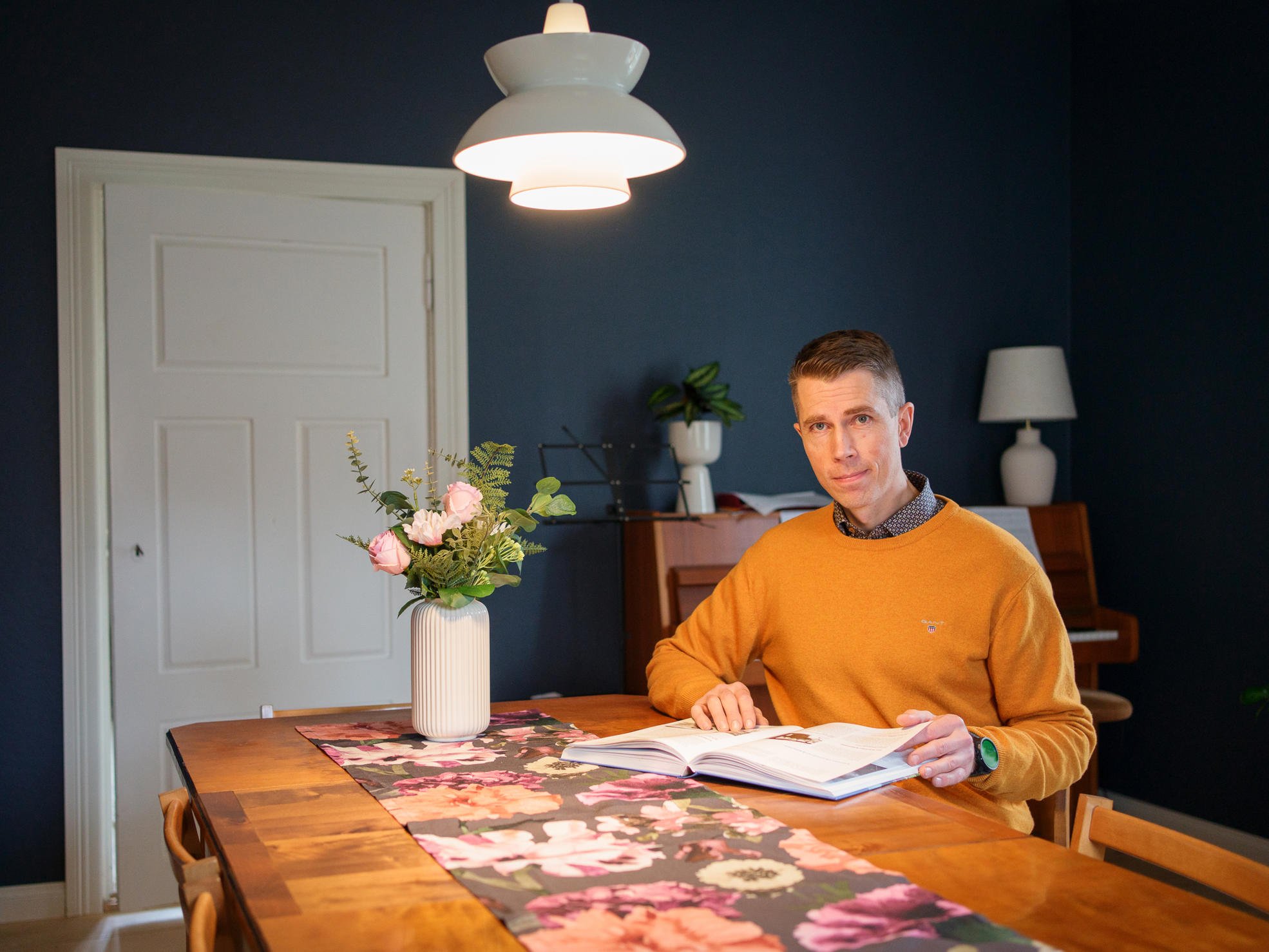 Ilkka Köntti istuu pöydän äärellä ja selaa kirjaa.