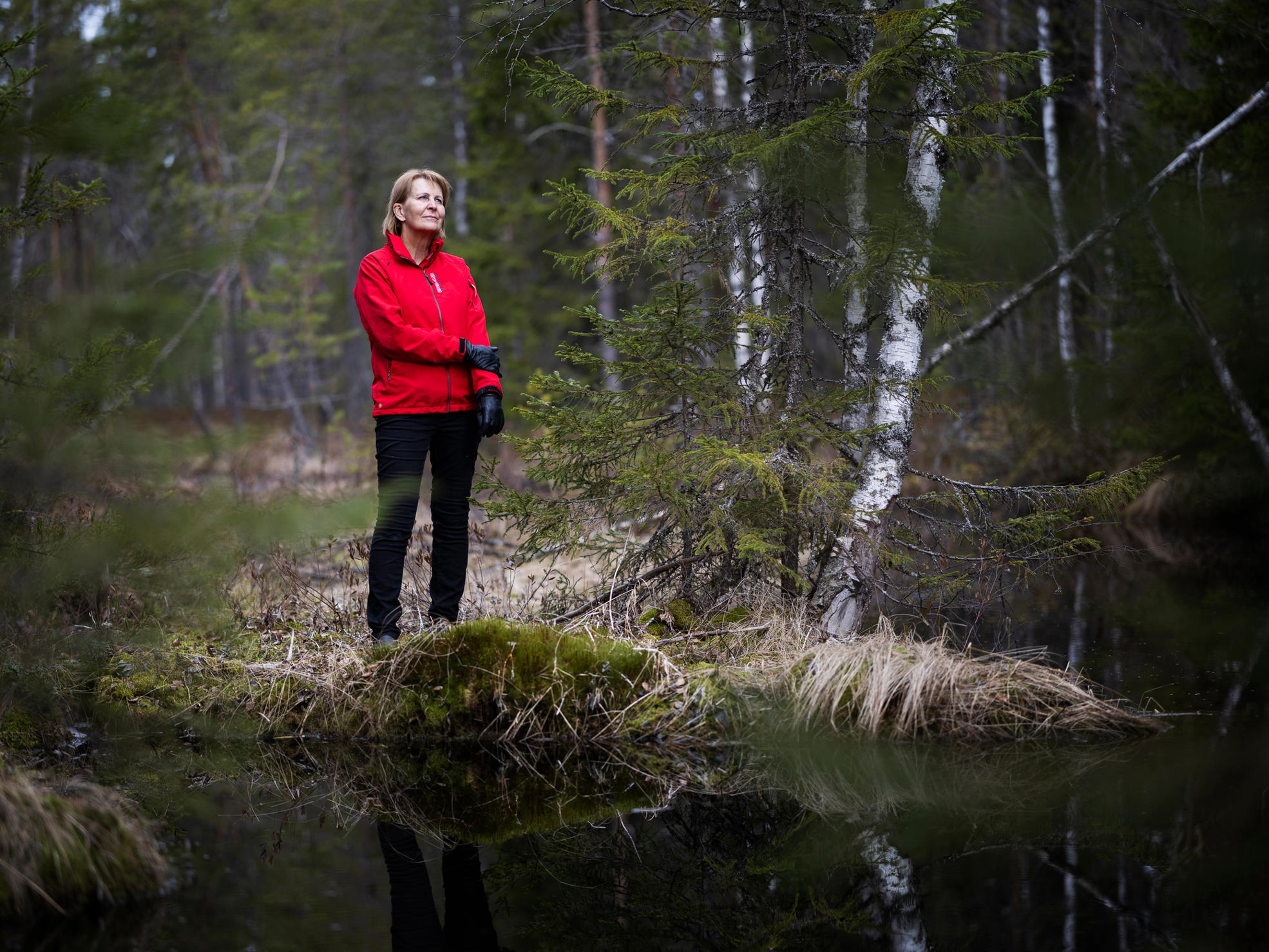 Skogsägaren står i skogen vid stranden av ett vattendrag.
