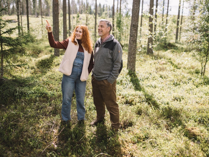 Far och dotter står i skogen och tittar i den riktning som fadern visar.