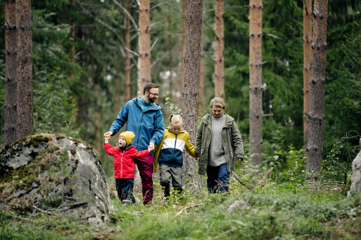 Isoäiti, isä ja lapset kävelevät metsässä kohti kameraa.