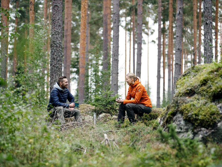 Skogsägare och skogsexpert sitter i samspråk i skogen på kaffe.