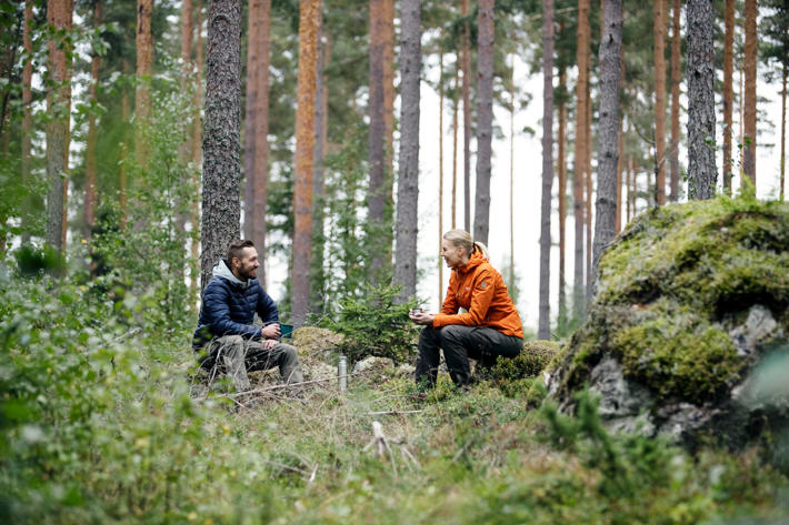 Metsänomistaja ja metsäasiantuntija istuvat metsässä juomassa kahvia ja juttelemassa.