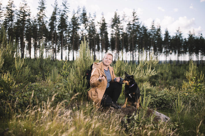 A woman kneeling by her dog in a stand of pine seedlings.