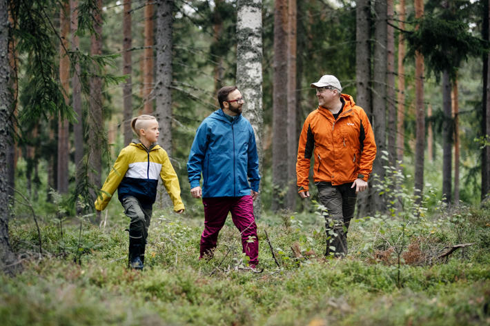 Metsäasiantuntija kävelee metsässä isän ja tämän pojan kanssa.