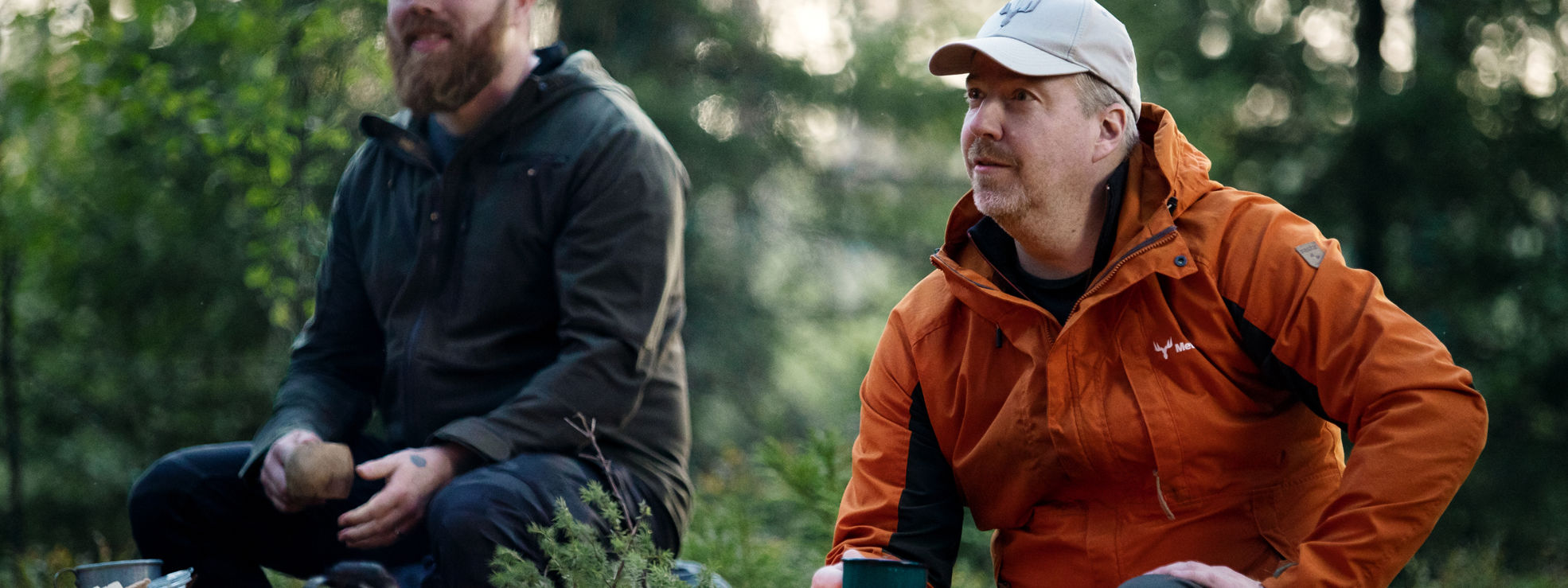 A forest owner and forest specialist sitting in the forest, enjoying coffee by the fire