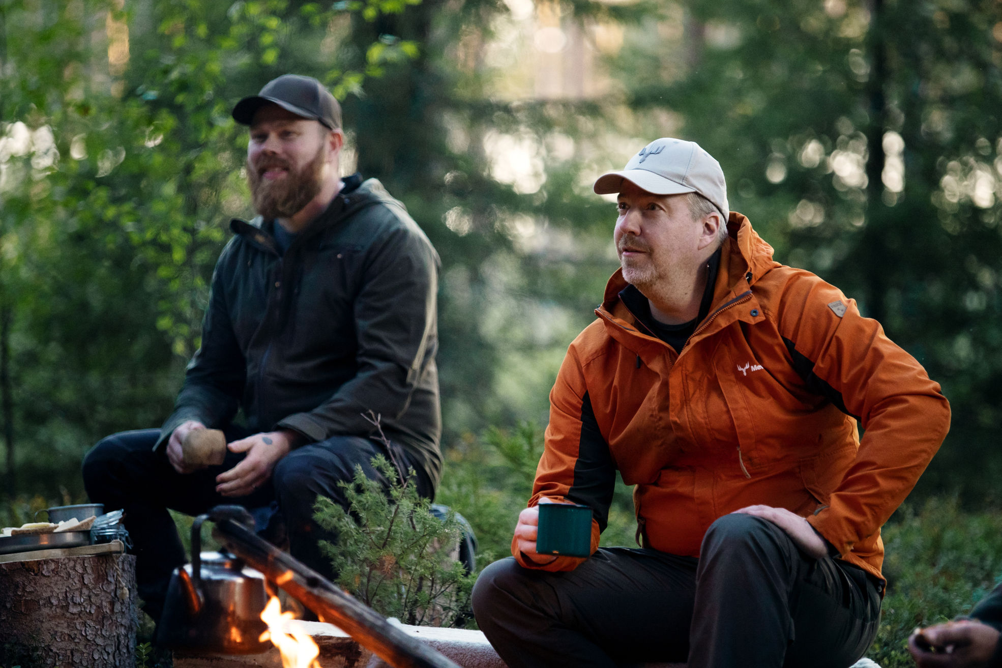 A forest owner and forest specialist sitting in the forest, enjoying coffee by the fire