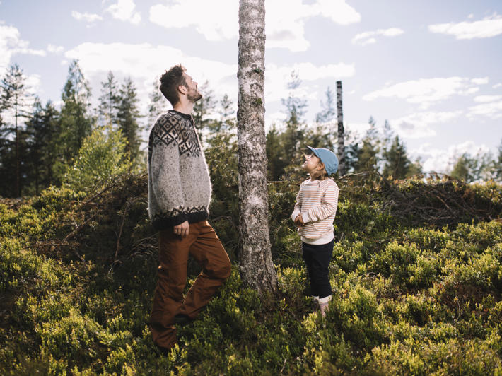 En vuxen och ett barn tittar på en konstgjord högstubbe i skogen.